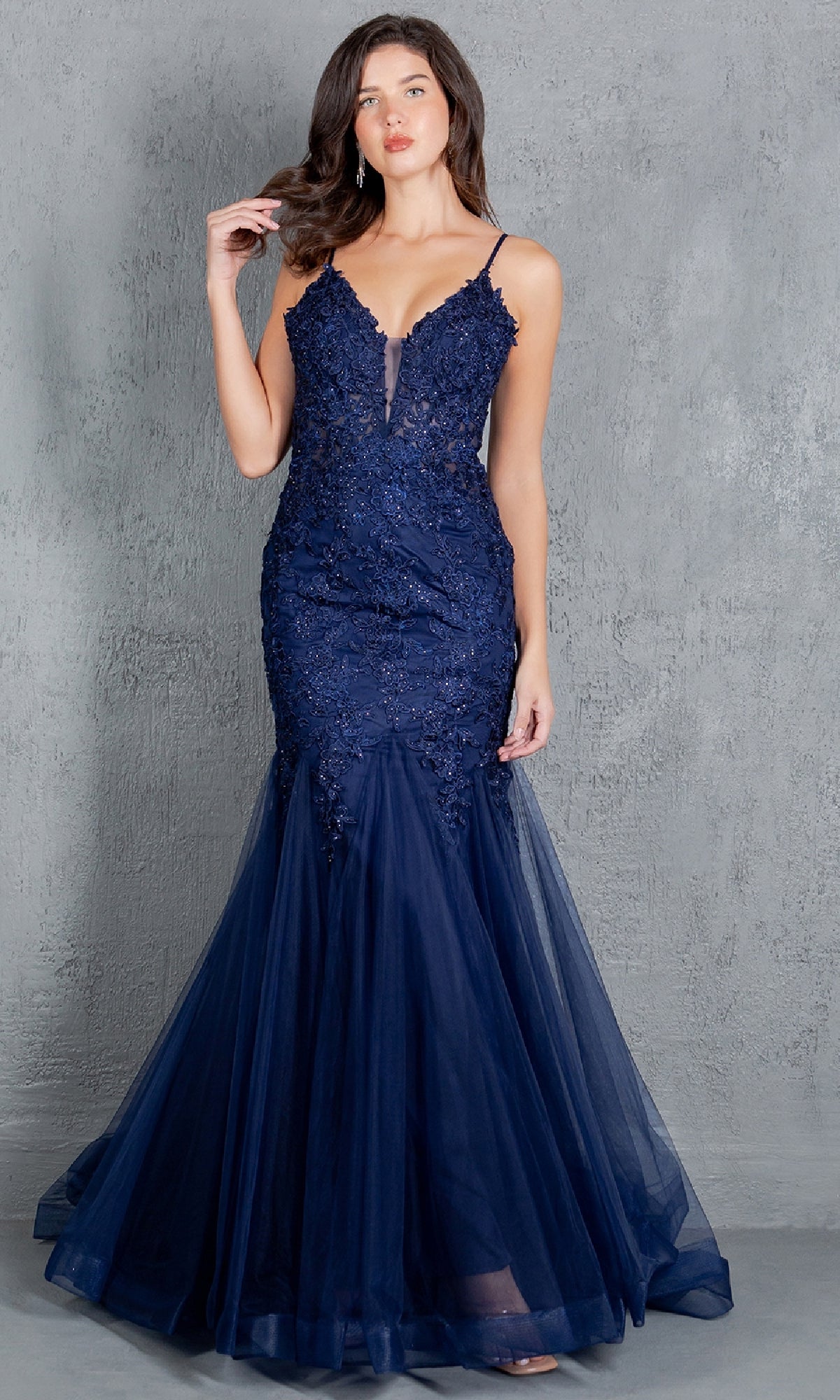A woman stands against a gray textured background, wearing the Cinderella Couture 8178J: a navy blue, floor-length mermaid prom dress with lace, tulle details, and beaded embroidery.