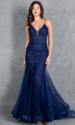 A woman stands against a textured gray wall wearing the Beaded Long Prom Dress: Cinderella Couture 8178J, a navy blue sleeveless mermaid gown with lace, tulle accents, and elegant beaded embroidery.