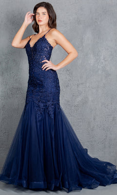 A woman stands before a gray textured wall wearing the Beaded Long Prom Dress: Cinderella Couture 8178J, a navy blue mermaid gown with thin straps, lace and tulle layers, and delicate beaded embroidery.