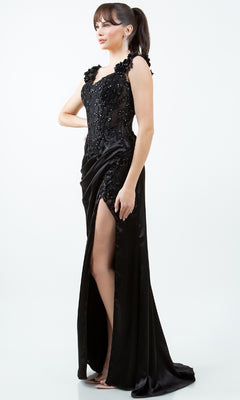 A woman stands against a plain white background wearing the Sparkly Long Prom Dress: Cinderella Couture 8181J, a black off-the-shoulder, floor-length gown featuring sequin embellishments and a high slit.