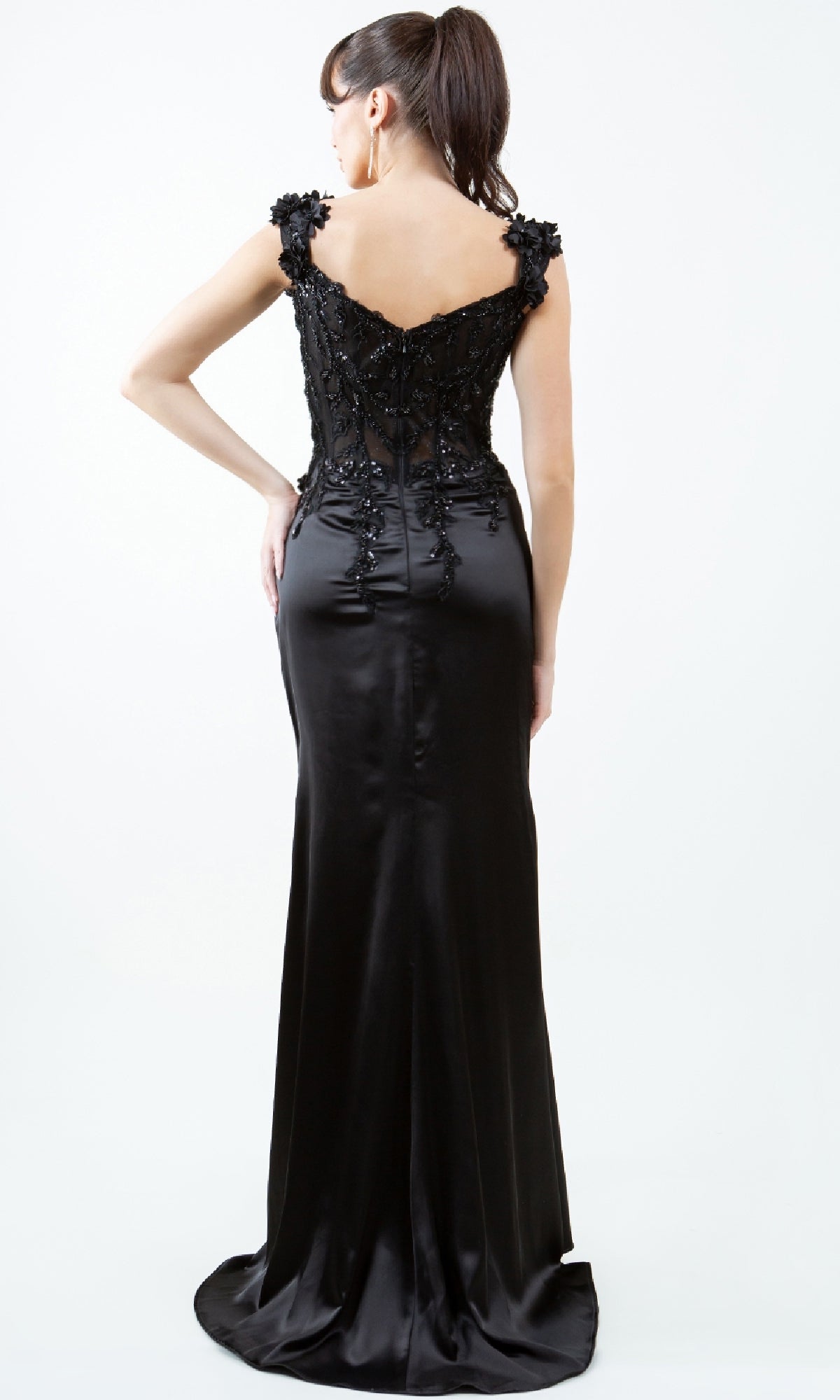 A woman stands facing away, wearing the Sparkly Long Prom Dress: Cinderella Couture 8181J, featuring ornate embroidery on the upper back and shoulders. This fitted black gown exudes elegance, ideal for any special occasion.