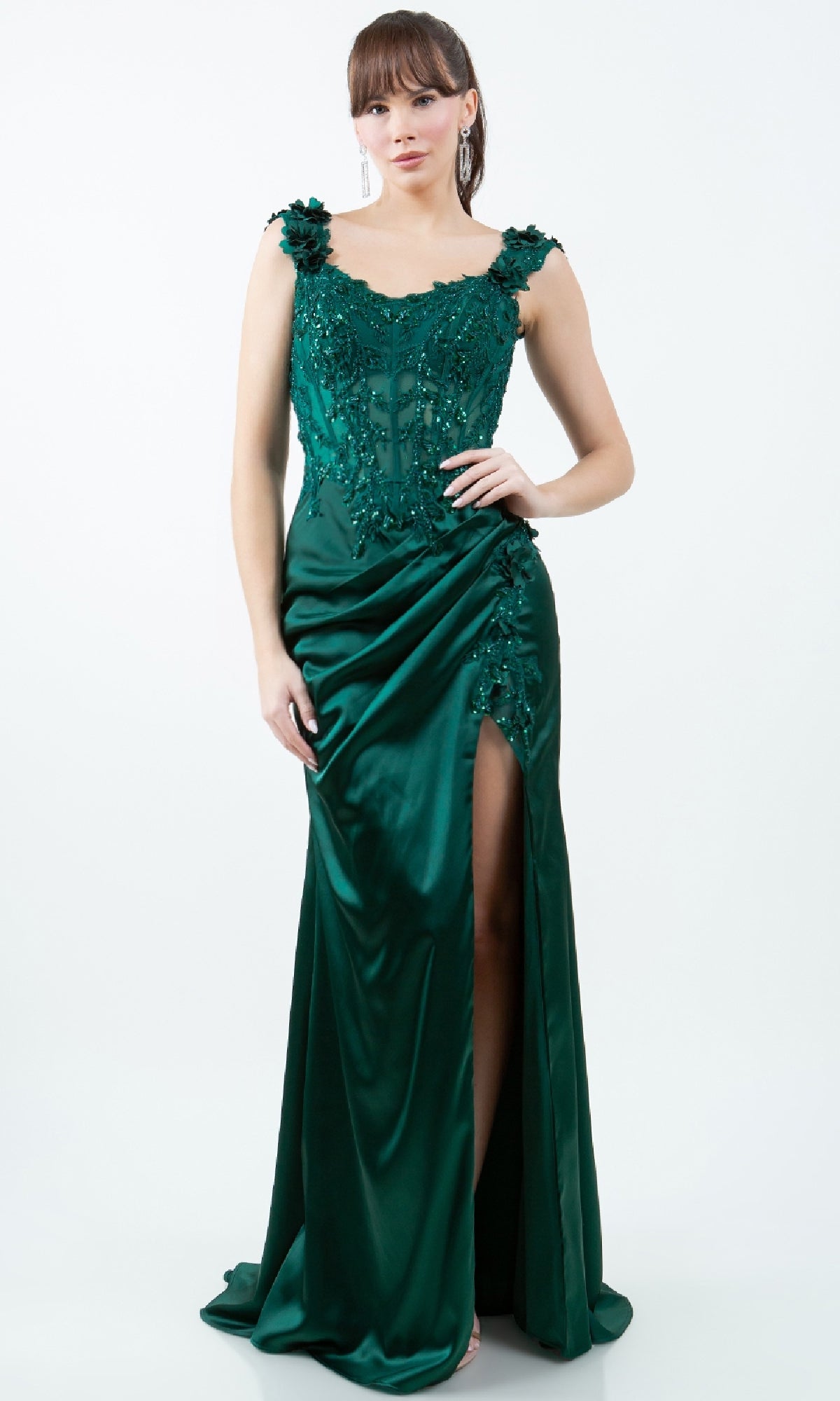 A woman wears the Sparkly Long Prom Dress: Cinderella Couture 8181J—an affordable emerald green, sleeveless, floor-length gown with lace, sequin details, and a high slit—posing against a white background.