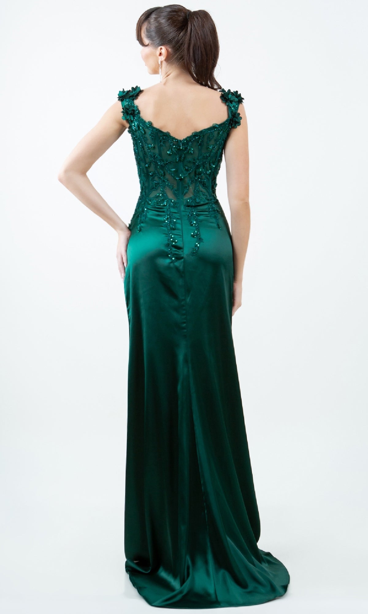A woman stands facing away, showcasing the stunning back details of the Sparkly Long Prom Dress: Cinderella Couture 8181J in dark green with floral embellishments and floor-length embroidery.