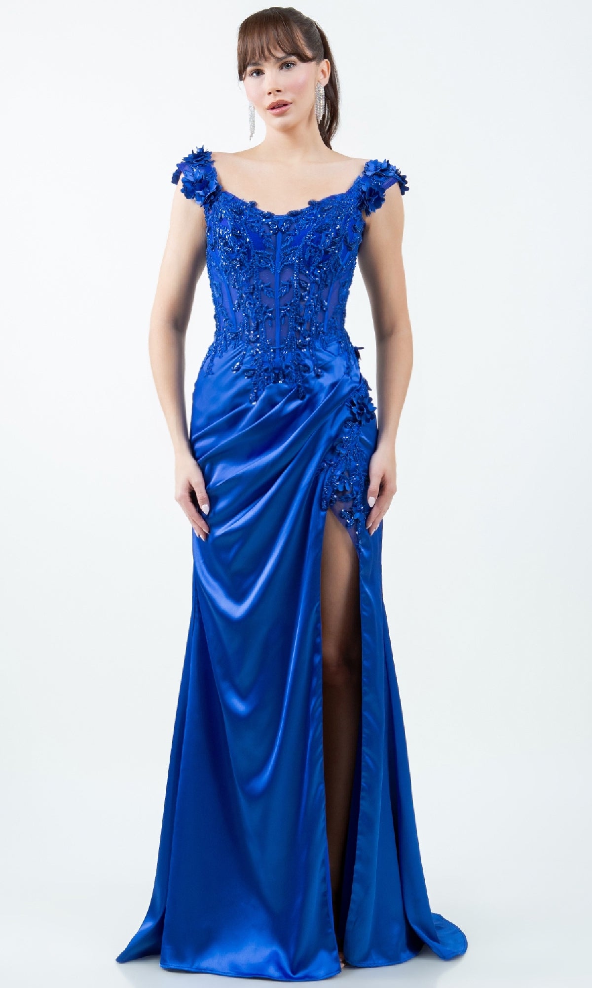 A woman wearing the Sparkly Long Prom Dress: Cinderella Couture 8181J in bright blue, featuring an off-the-shoulder design, floral appliqués, bead embellishments, and a thigh-high slit.