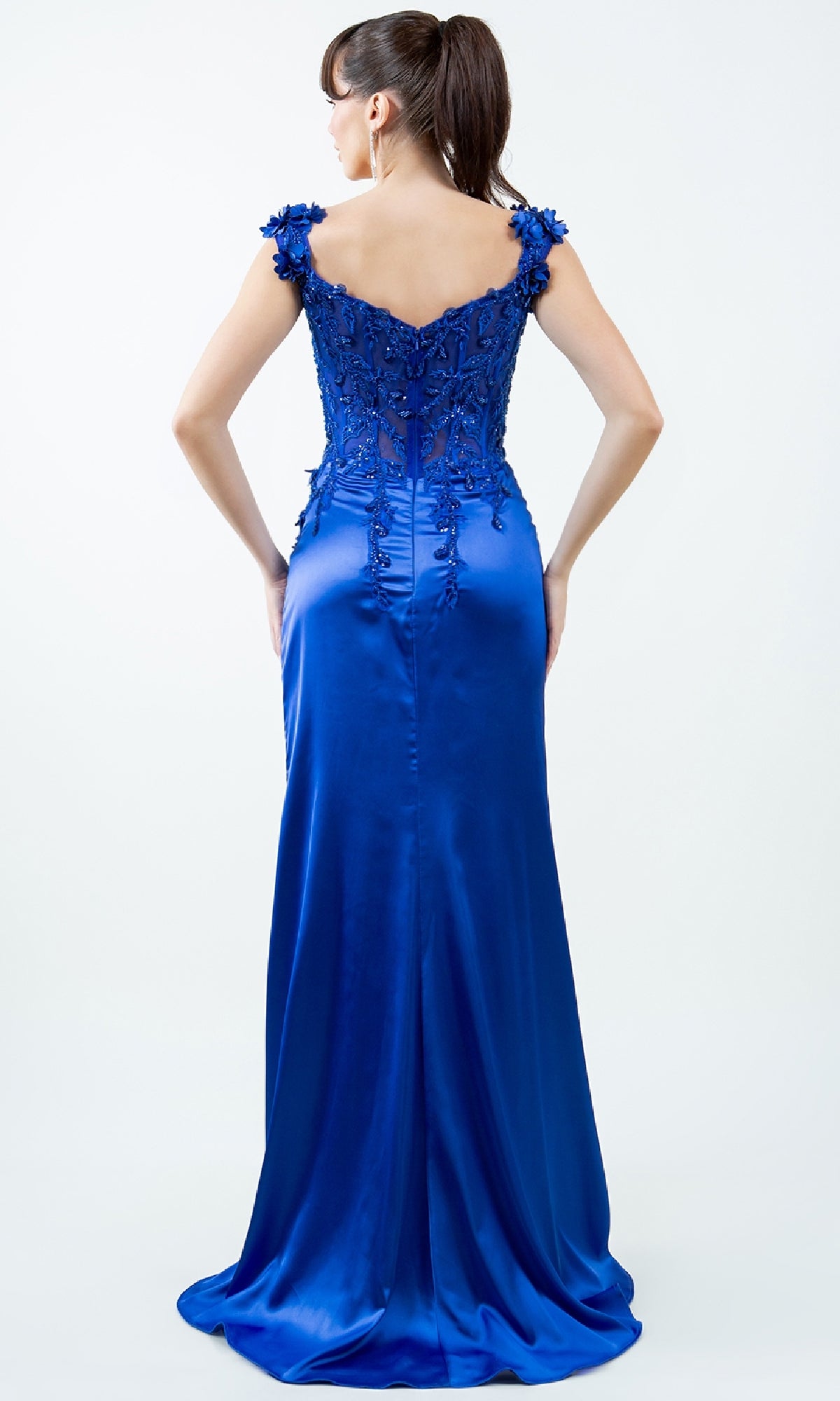 Woman wearing the Sparkly Long Prom Dress: Cinderella Couture 8181J—a vibrant blue, floor-length gown with a fitted floral lace bodice and cap sleeves—shown from the back against a plain light background.