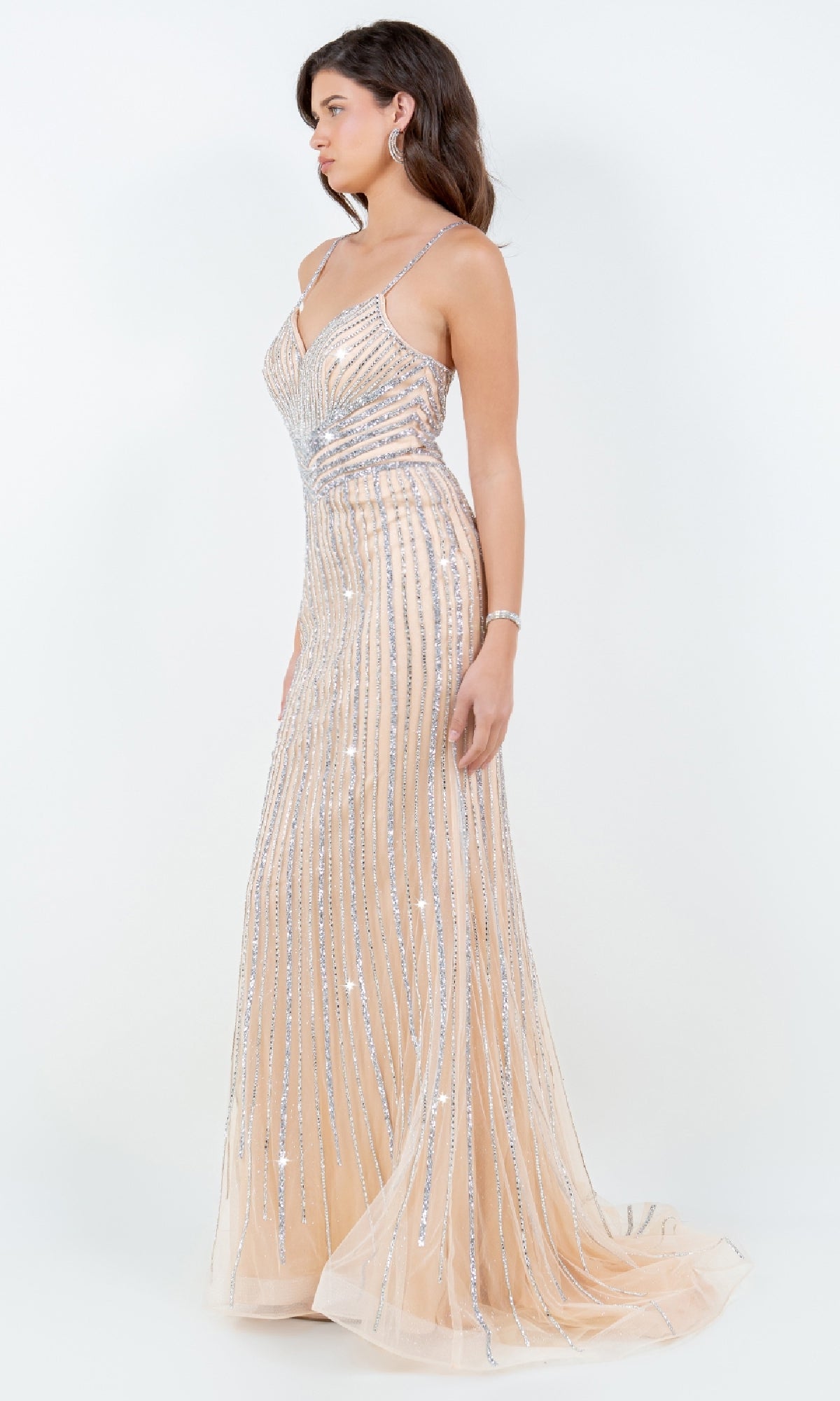 A woman models the Cinderella Couture 8203J Bead-Striped Prom Gown, a floor-length, sleeveless dress with thin straps and silver bead stripes on nude sheer fabric, posing against a plain white background.