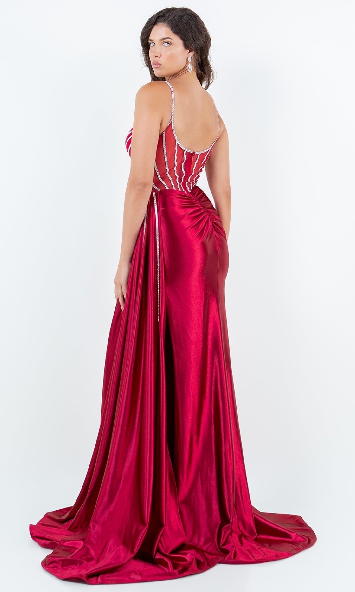 Woman in a sleeveless, floor-length red Side-Sash Long Prom Gown by Cinderella Couture 8219J with rhinestone straps and beaded detailing, shown facing away and glancing over her shoulder against a white background.