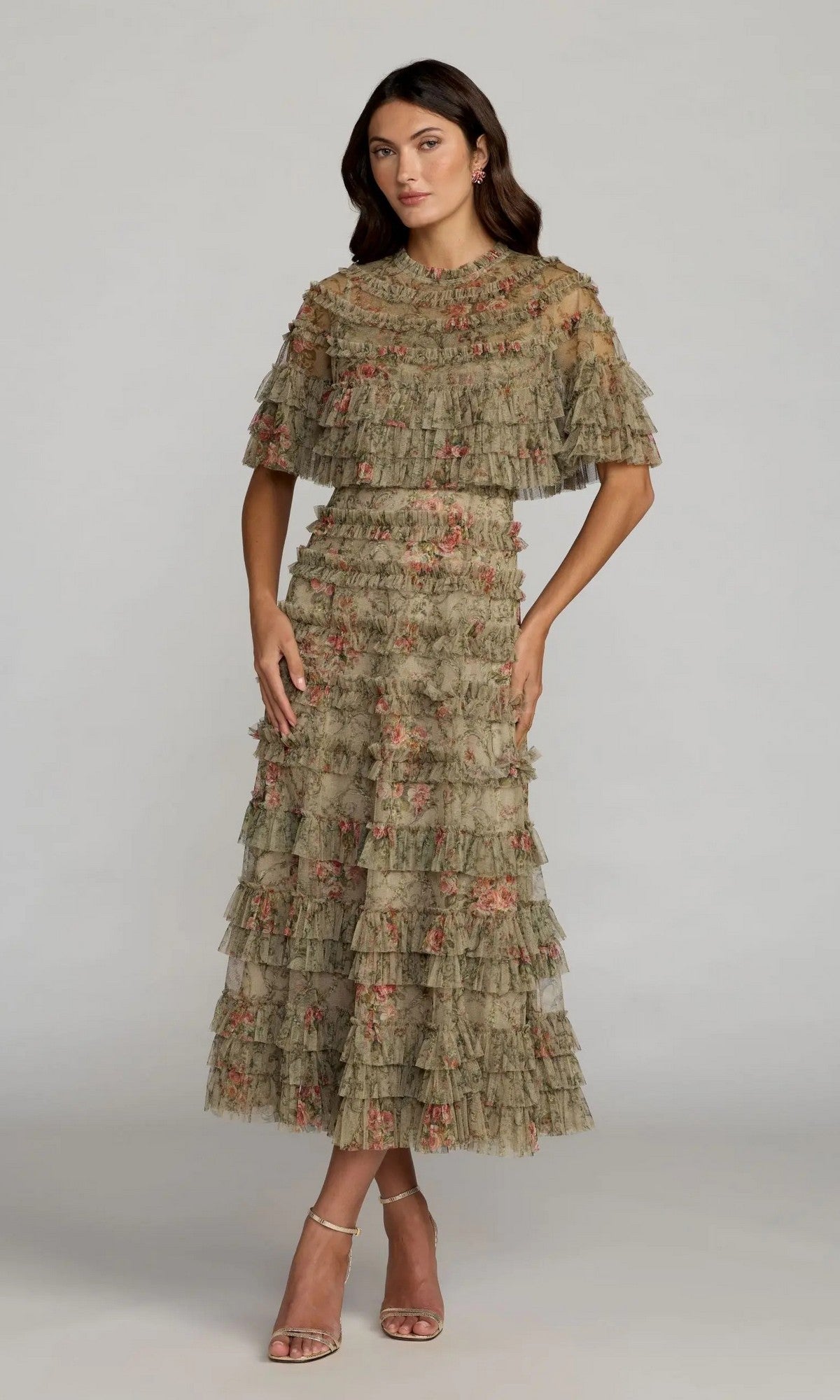 A woman stands against a plain grey background wearing the Mac Duggal 8231 tea-length party dress in olive, featuring floral details and short sleeves, paired with nude heeled sandals.