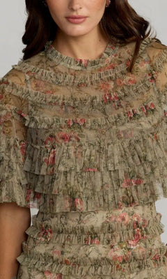 A woman wearing the Tea-Length Party Dress: Mac Duggal 8231, a sheer, vintage-inspired dress adorned with floral embroidery in pink and olive-green tones, featuring layered ruffles and short sleeves.