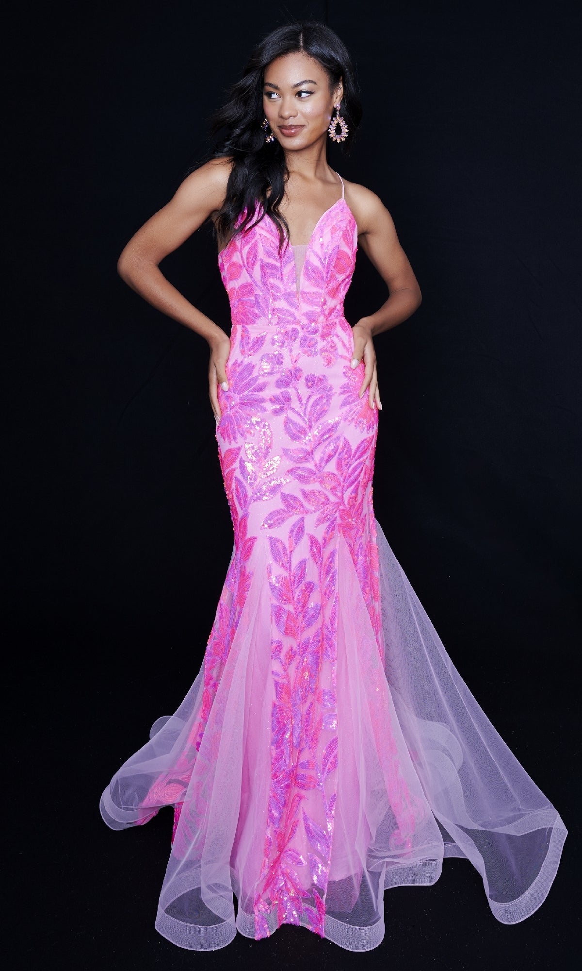A woman poses elegantly in the Nina Canacci 8236, a floor-length pink sequin mermaid gown with leaf patterns and tulle accents, set against a black background.