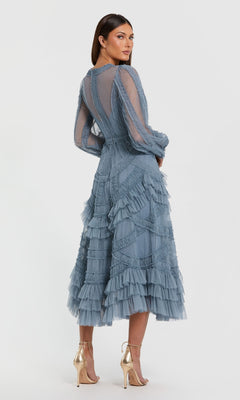 Woman wearing the Blue Midi Wedding Guest Dress: Mac Duggal 8247—a sheer, long-sleeved blue midi dress with ruffled tiered layers—stands in profile, styled with metallic high-heeled sandals for an elegant occasion-ready look.