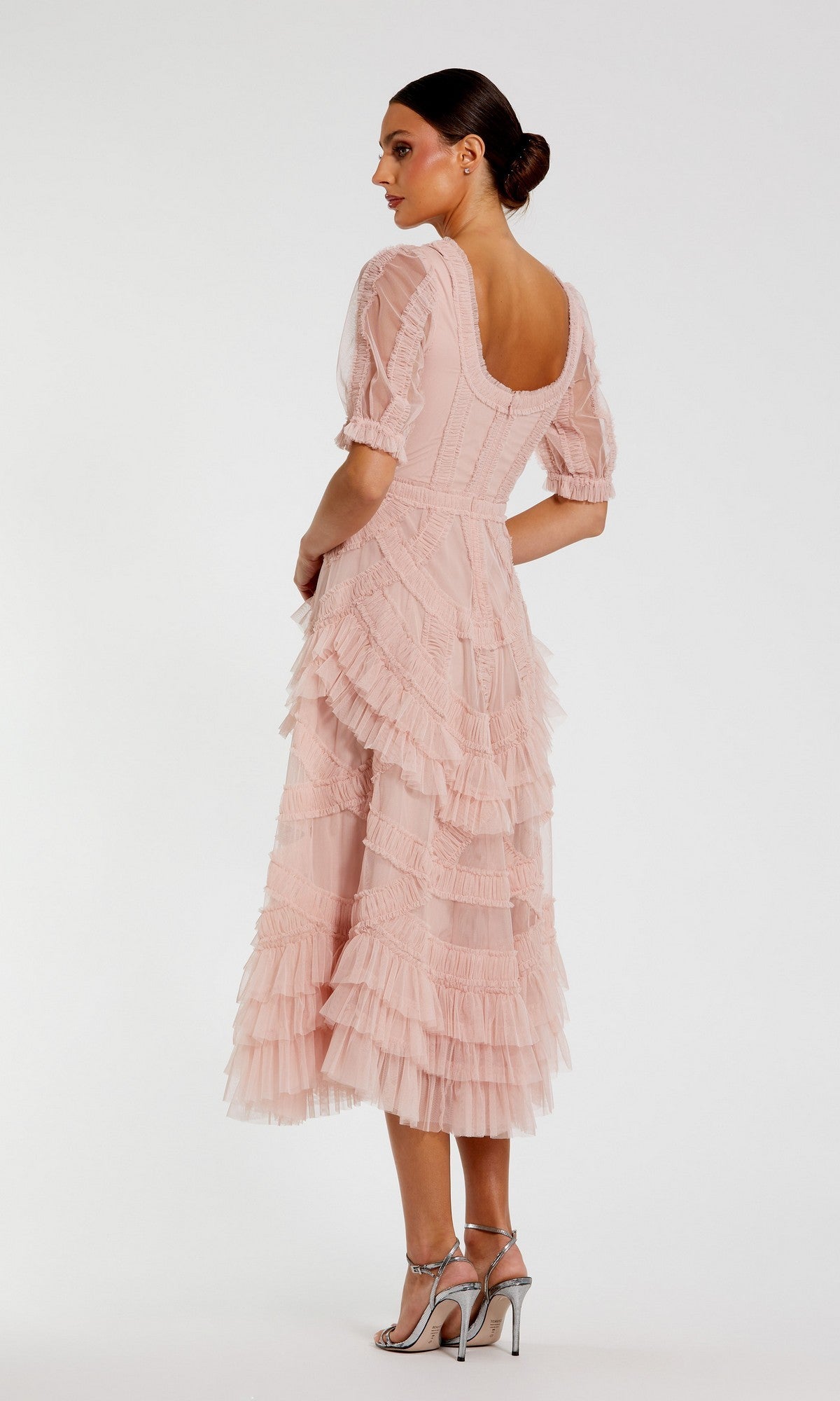 A woman faces away, wearing the Mac Duggal 8248 Ruffled Midi Wedding Guest Dress in light pink with short sleeves and silver heels—ideal for semi-formal events or as a wedding guest dress against a plain background.