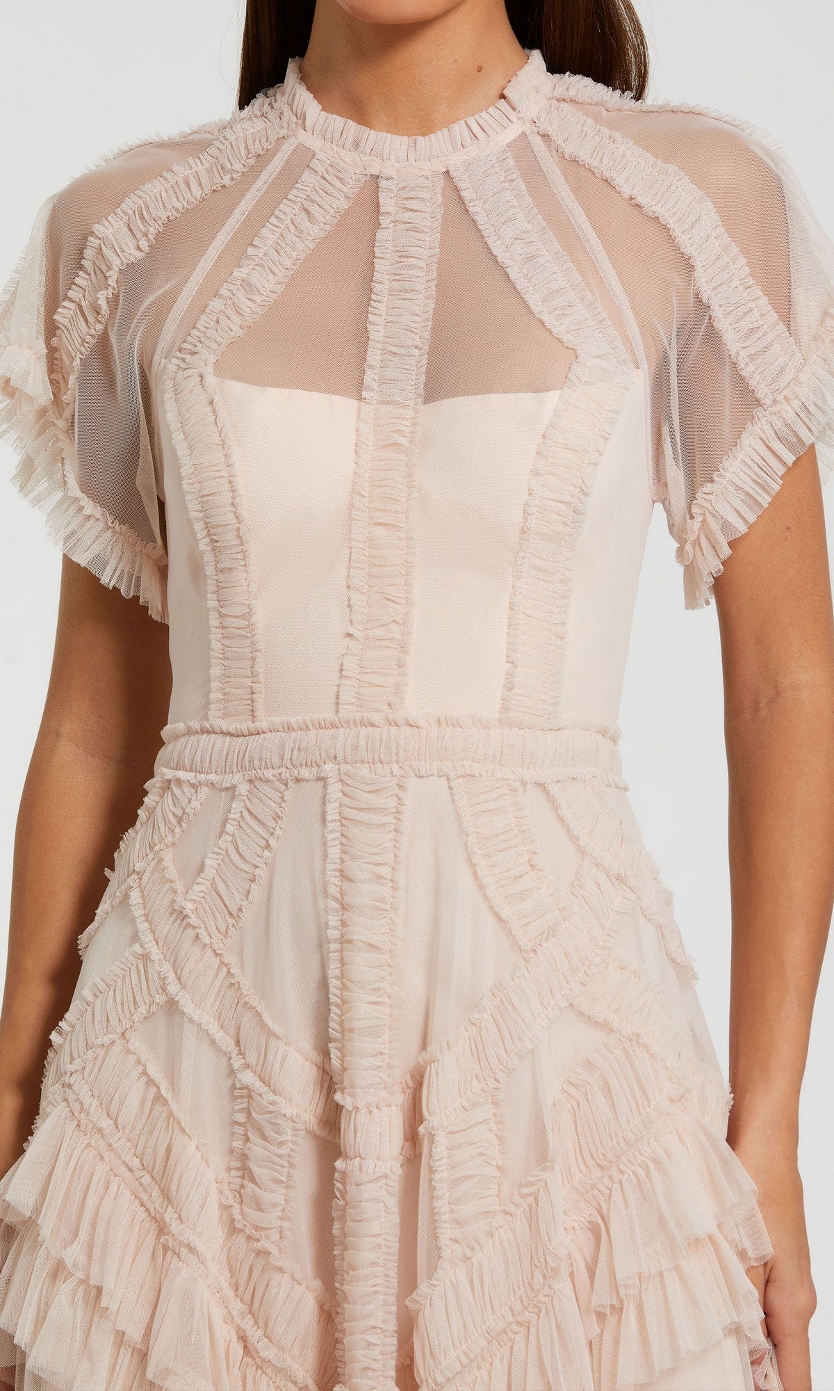 A woman wearing the Tea-Length Party Dress: Mac Duggal 8249, a short-sleeved, light pink midi dress featuring sheer panels, ruffled trim, and geometric detailing on the bodice and skirt—an elegant choice perfect for any special occasion.