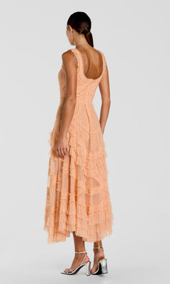 A woman faces away, wearing the Mac Duggal 8250 midi wedding guest dress with micro ruffle detailing and silver high-heeled sandals, set against a plain light gray background.