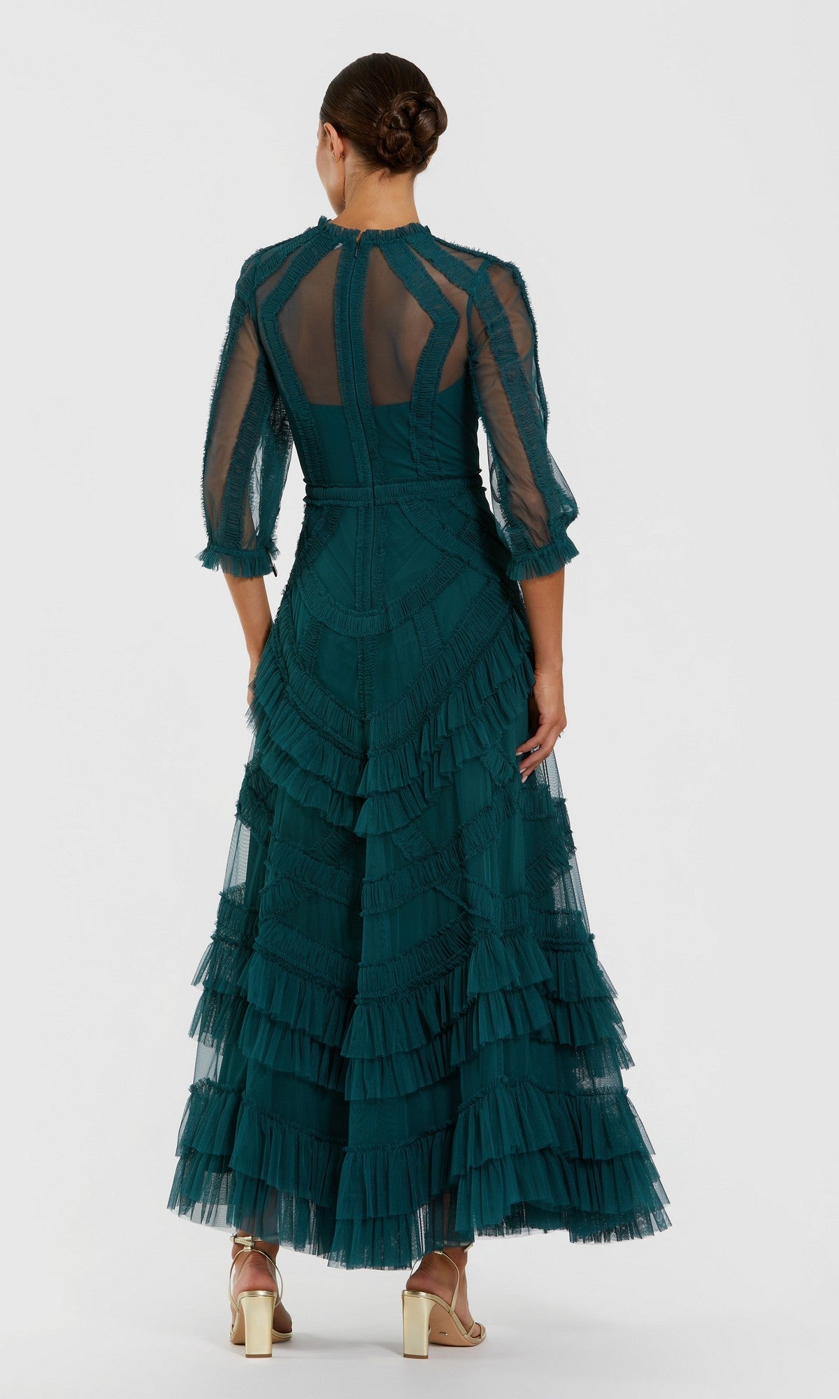 A woman faces away in the Mac Duggal 8251 long formal dress—teal, ankle-length, with ruffles and sheer sleeves. Her hair is in a low bun, paired with heeled sandals, creating an effortlessly elegant look.