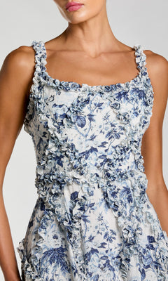A woman wears the Floral Wedding Guest Dress: Mac Duggal 8256, a blue floral print design with ruffle trim on the bodice and straps and an elegant A-line skirt—ideal for a stylish wedding guest look.