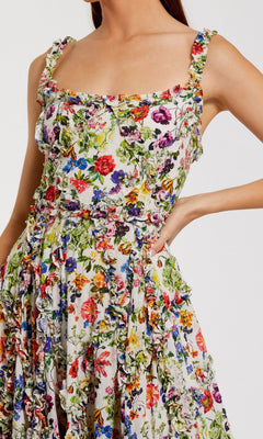 A woman poses with one hand on her hip, wearing the Mac Duggal 8256 Floral Wedding Guest Dress, a sleeveless ruffled scoop-neck dress with a colorful floral pattern.