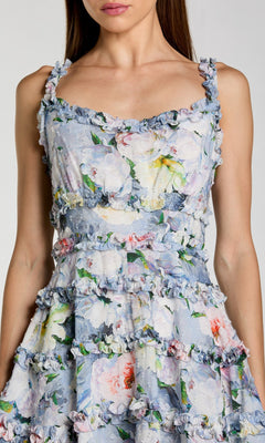 Woman wearing the Mac Duggal 8257 short party dress, featuring sleeveless design, floral print, ruffled trim, and tiered layers. Shown from shoulders to above the knees.