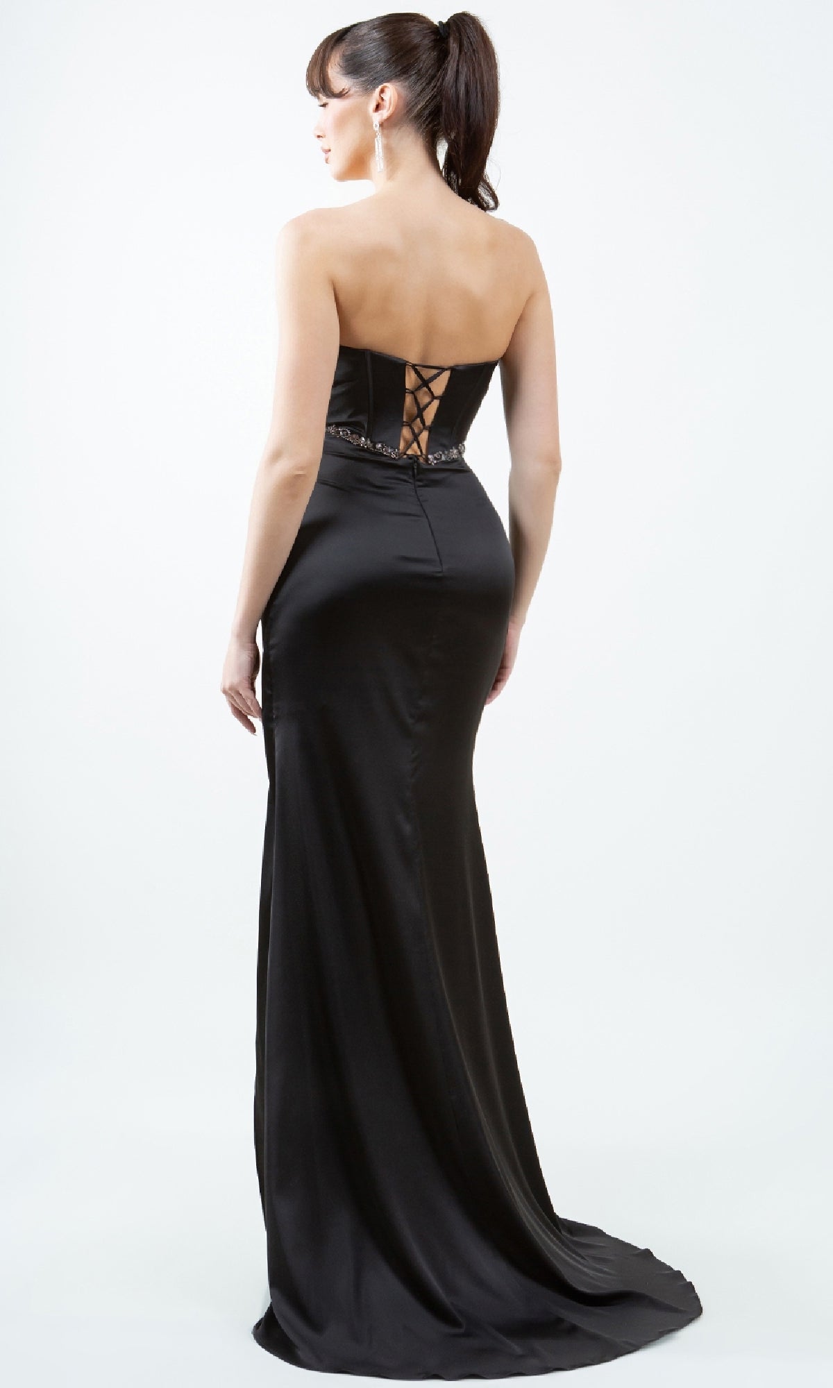A woman stands facing away from the camera in a Cinderella Couture 8259J strapless long prom gown, featuring a black, floor-length skirt and corset-style lace-up back, set against a plain white background.