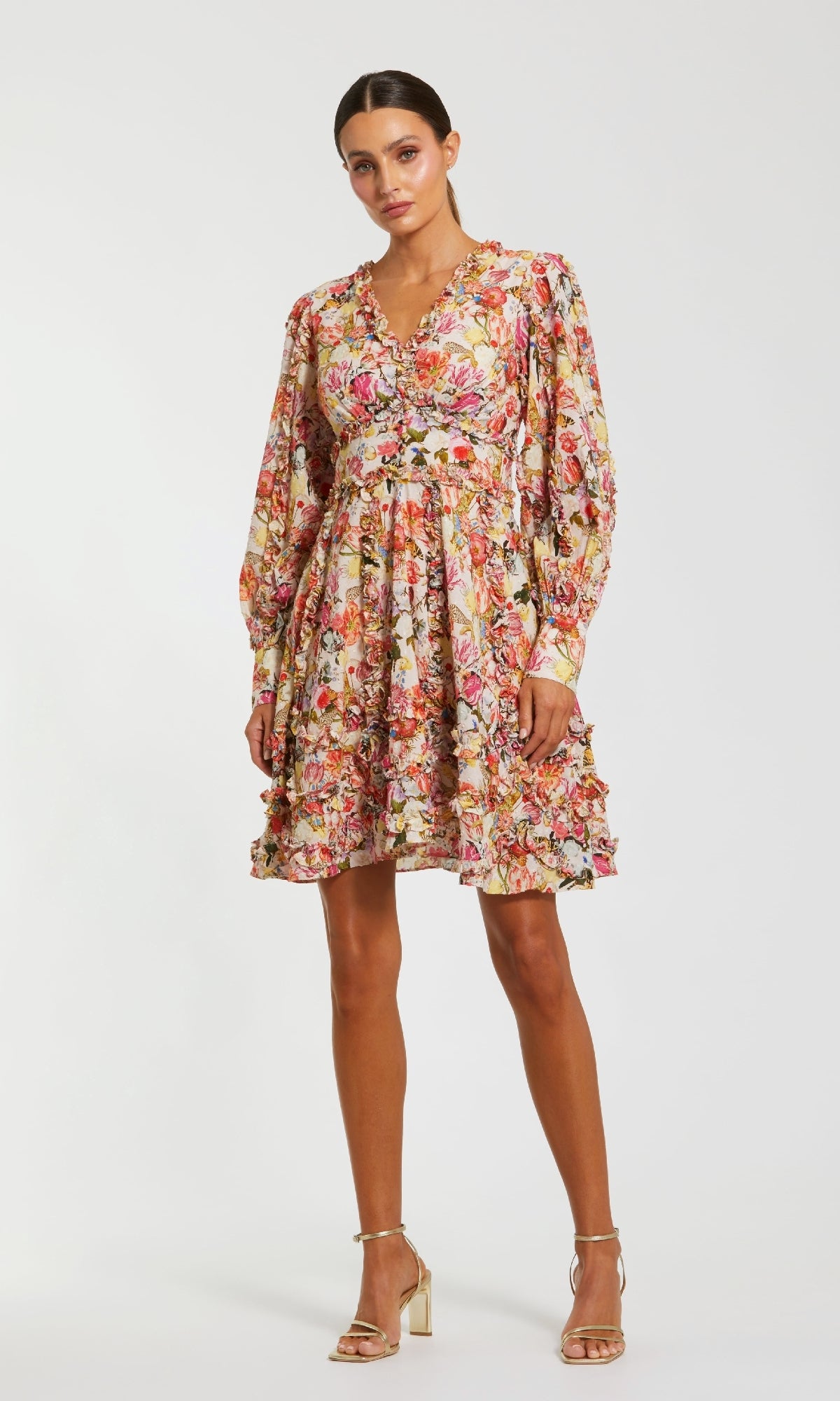 Woman wearing the Mac Duggal 8261 Micro-Ruffle Wedding-Guest Dress, a long-sleeved, knee-length floral-print style with ruffle details, standing against a plain white background.