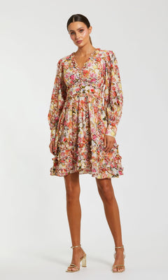 Woman wearing the Mac Duggal 8261 Micro-Ruffle Wedding-Guest Dress, a long-sleeved, knee-length floral-print style with ruffle details, standing against a plain white background.