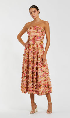 A woman wears the Mac Duggal 8262 Midi Floral Wedding Guest Dress in pink, red, and peach tones, styled with metallic high-heeled sandals—an elegant choice for attending a wedding.