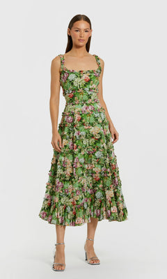 Woman in the Mac Duggal 8263 Midi Wedding Guest Dress in Green Multi with a fitted bodice and ruffled skirt, paired with silver strappy heels, standing against a plain background.