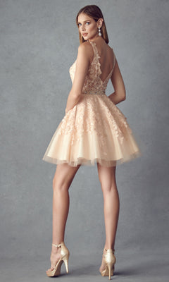 A woman stands sideways against a gray background, wearing the Short Hoco Dress: Juliet 826 featuring a light pink lace bodice and sheer back, paired with gold high-heeled sandals.
