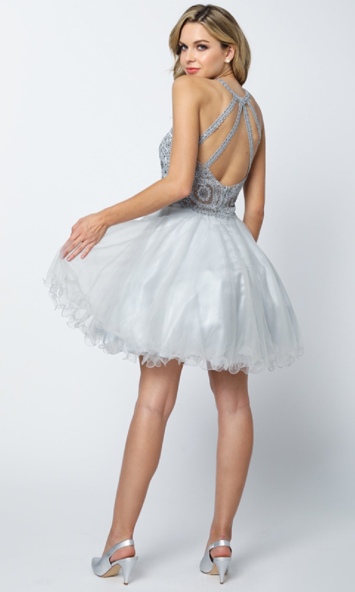 A woman wears the Juliet 826 Short Hoco Dress with a fitted embellished bodice, open strappy back, and A-line tulle skirt, paired with silver high heels.
