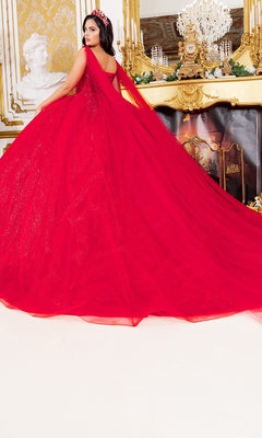 A woman stands in an ornate room adorned with gold accents, a fireplace, and a chandelier, wearing the Quinceanera Dress 8270J By Cinderella Couture—a voluminous red ball gown with a sparkling tulle skirt that radiates fairy-tale elegance.