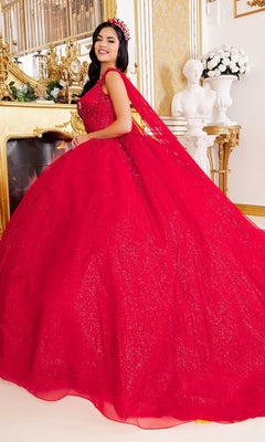 A woman wearing the Quinceanera Dress 8270J By Cinderella Couture—a sparkling red ball gown with elegant cape sleeves and a tiara—stands in an ornate room adorned with gold accents, a fireplace, and a white statue in the background.