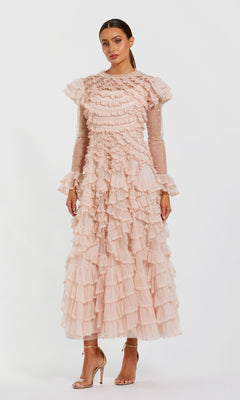 A woman models the Mac Duggal 8274 Long Sleeve Ruffle Formal Dress in light pink with sheer sleeves and nude high-heeled sandals, posing against a plain white background.