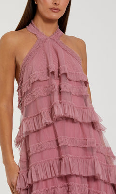 A woman wearing the Mac Duggal 8276 Tea-Length Party Dress, a sleeveless halter mesh ruffle dress featuring multiple layers of pink fabric and a chic high-low hemline, stands against a plain background.