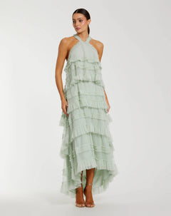 A woman wearing the Tea-Length Party Dress: Mac Duggal 8276 in Seamist, featuring a halter mesh ruffle design and high-low hemline, paired with strappy heels and standing against a plain white background.