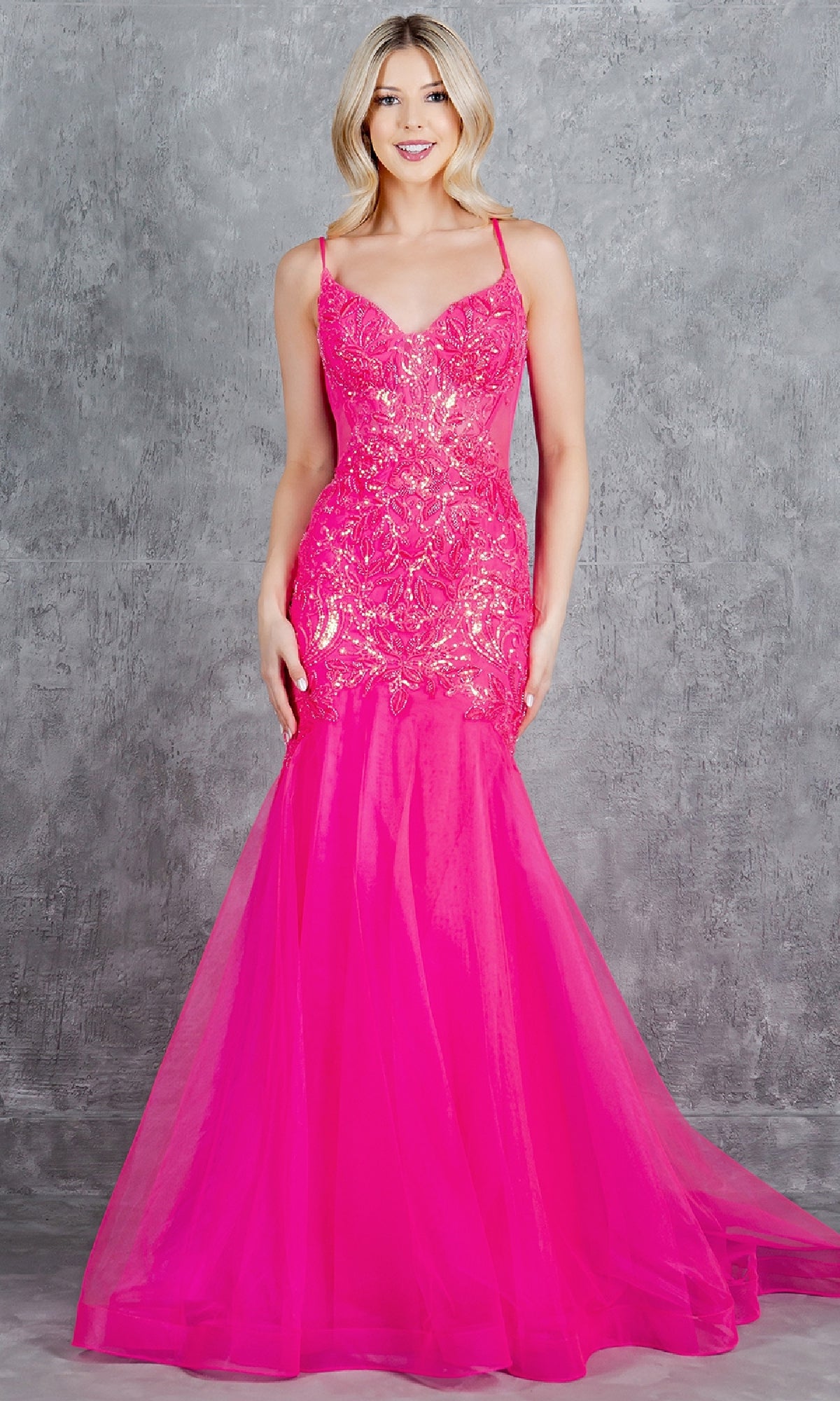 A woman wearing the Long Mermaid Prom Dress, Cinderella Couture 8276J, a sleeveless hot pink sequin gown with a fitted bodice and flared tulle skirt, stands before a gray textured background.