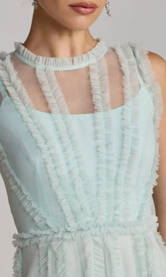 A woman wearing the Mac Duggal 8289 Short Ruffled Wedding Guest Dress—a sleeveless light blue dress with sheer paneling and vertical ruffle details, perfect for a semi-formal party.