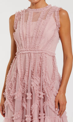A woman wears the Mac Duggal 8289 short wedding guest dress, a light pink sleeveless mini with ruffled trim and sheer panel detailing.