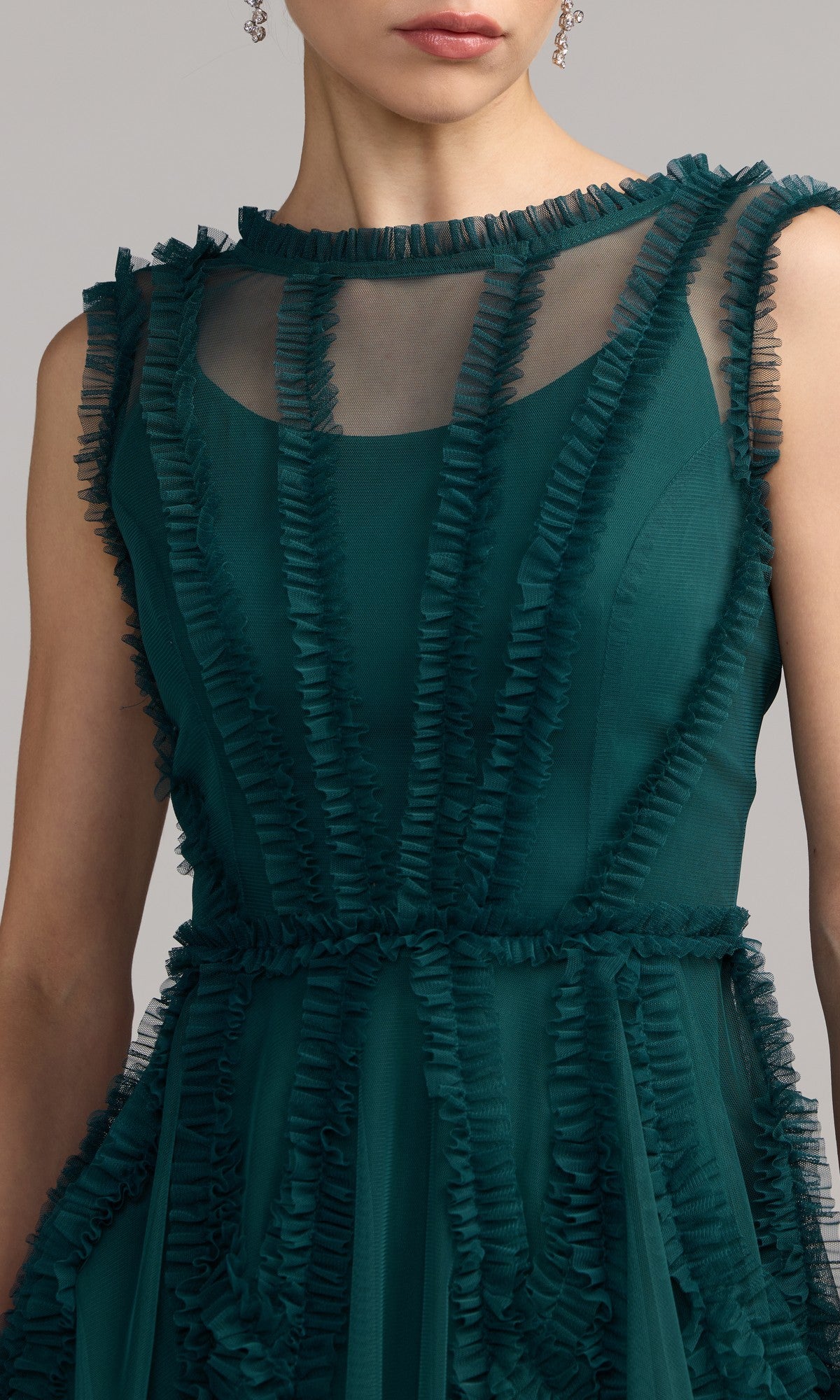 A woman wearing the Mac Duggal 8289 short ruffled wedding guest dress, a sleeveless dark green semi-formal style with sheer panels and ruffle trim.