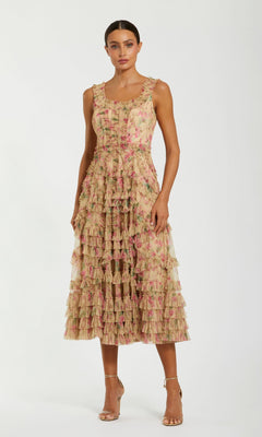 A woman is standing in the Mac Duggal 8293 Midi Party Dress, a sleeveless, beige multi A-line dress with pink floral patterns and layered ruffles, styled with gold high-heeled sandals.