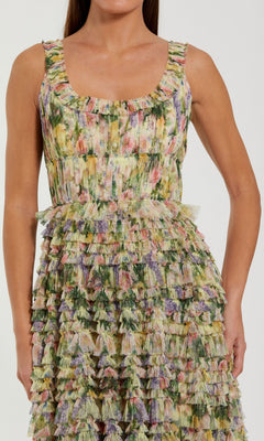 A woman is wearing the Mac Duggal 8299 Tea-Length Party Dress, a sleeveless style featuring a ruffled, multicolored floral pattern. The image captures her from shoulders to mid-thigh.