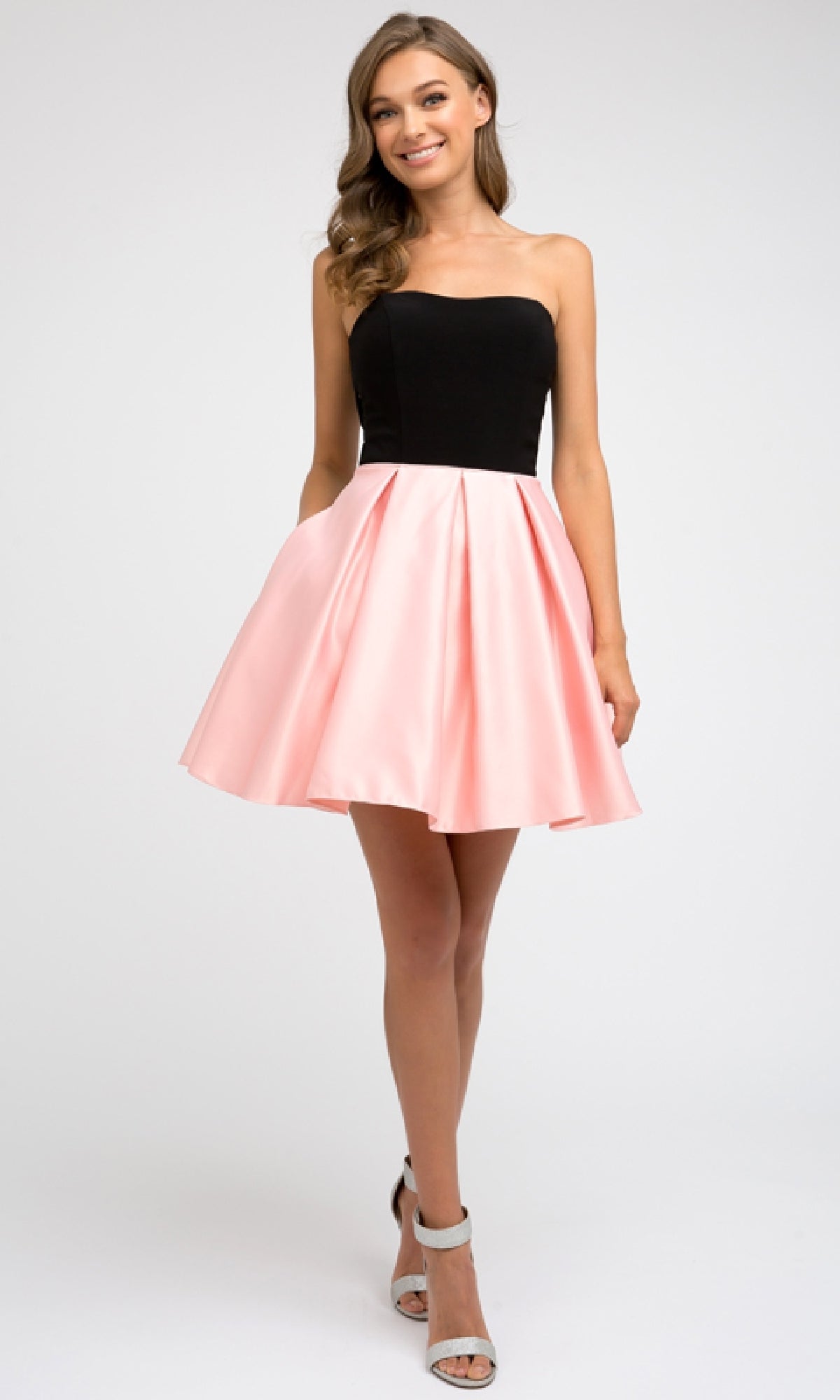 A woman stands facing forward, wearing the Juliet 829 short party dress with a strapless sweetheart neckline, an A-line pink knee-length skirt, and light-colored high heels.