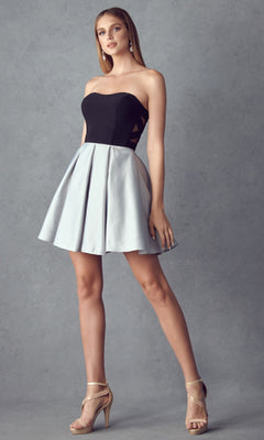 A woman poses against a gray background wearing the Juliet 829 short party dress with a strapless sweetheart neckline, black and gray A-line skirt, and beige high-heeled sandals.