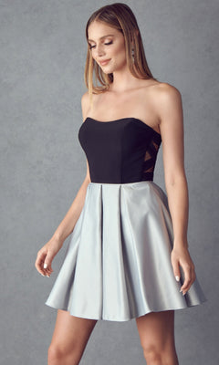 A woman stands against a gray background wearing the Short Party Dress: Juliet 829, featuring a strapless sweetheart neckline, black and silver color, fitted bodice, and flared A-line skirt.