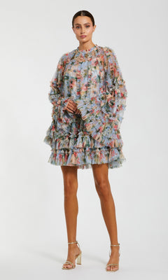 A woman wears the Mac Duggal 8300 Bell-Sleeve Floral Wedding Guest Dress, featuring sheer layers and ruffles, paired with metallic heels—a chic pick for a short wedding guest dress.
