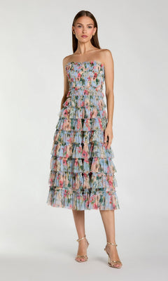 A woman wears the Mac Duggal 8301 Blue Multi floral wedding-guest dress with tiered midi layers and silver heels, standing against a plain background.