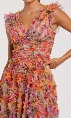A woman wears the Long Formal Dress: Mac Duggal 8303, a sleeveless floral gown with a V-neckline and colorful ruffled fabric in vibrant shades of pink, orange, purple, and yellow.