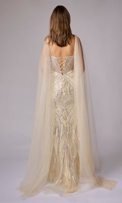A person stands facing away in the Nina Canacci 8305 long formal dress, featuring gold and silver embellishments, sheer cape sleeves, and a lace-up back, set against a plain background.