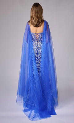 A woman faces away, wearing the Long Formal Dress: Nina Canacci 8305—an embellished gown with blue geometric patterns and a sheer, glittery cape cascading to the floor, perfect for formal evenings.