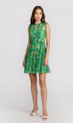 A woman stands against a plain background wearing a sleeveless Mac Duggal 8307 high-neck print wedding-guest dress in green floral and white open-toe heels.