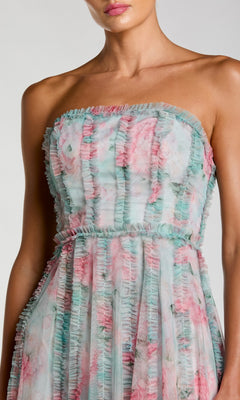 A woman wears the Mac Duggal 8308 Strapless Print Midi Party Dress, featuring pastel floral prints and vertical pleats on the bodice and skirt.